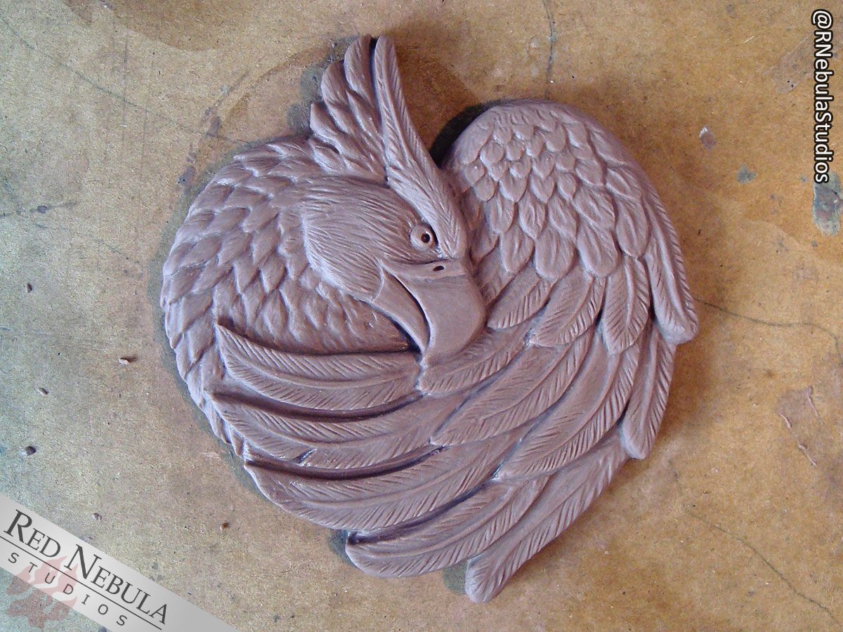 A sculpted griffon wall plaque in clay with detailed feathers.