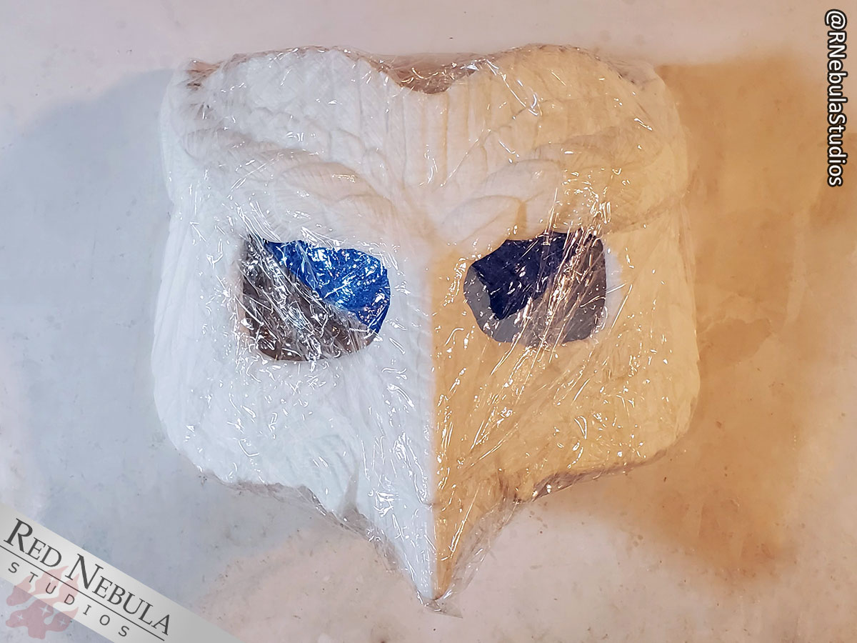 An owl mask wrapped in cellophane, ready to be covered in clay to create a matrix mold.