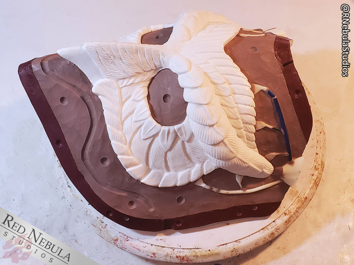 The resin owl mask in the first half of the matrix mother mold, with a layer of clay around the outside forming half of the final mold cavity.