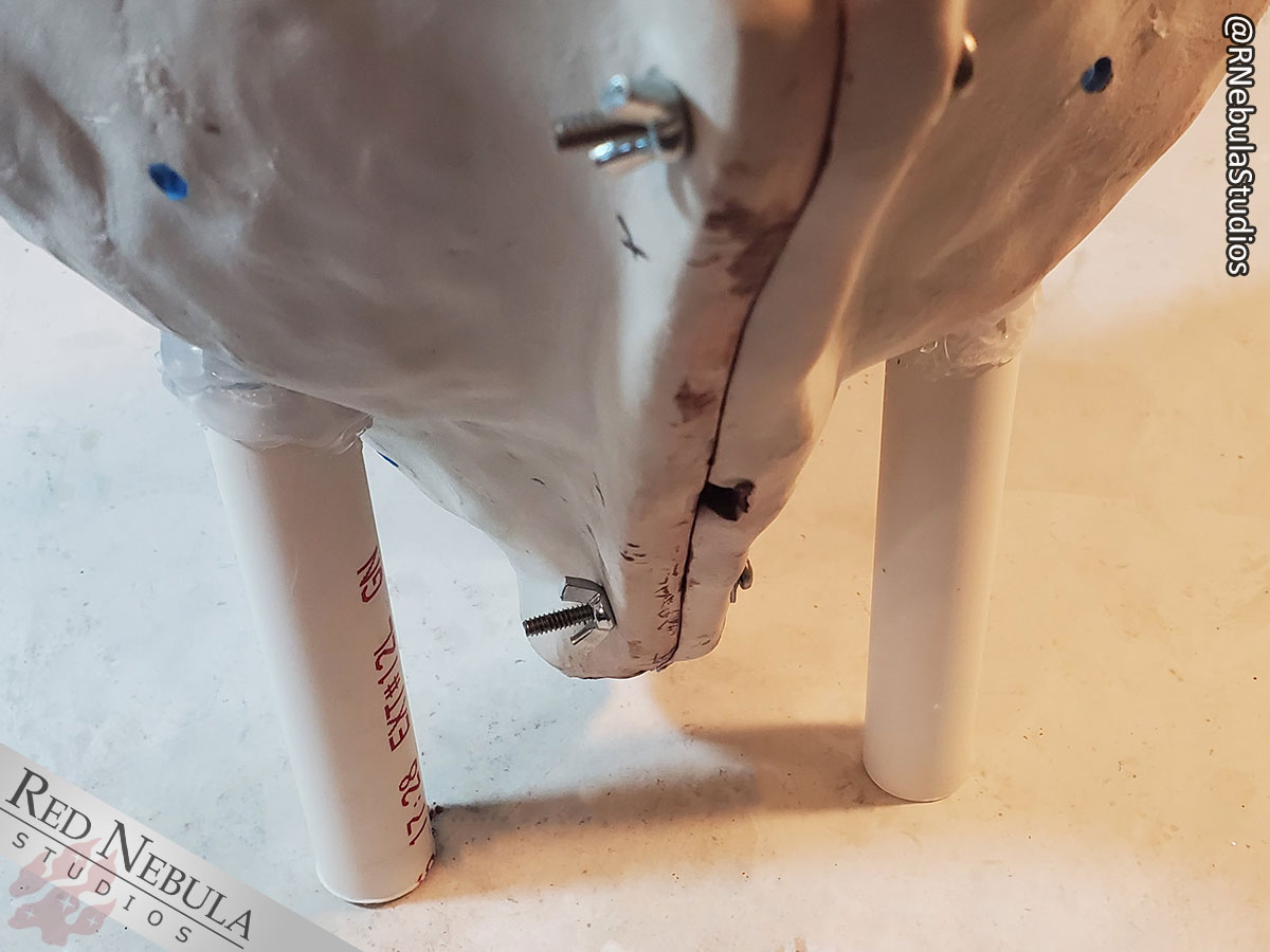 A pair of support structures made of PVC pipe have been hot glued onto the front half of the mold to allow it to stand upright when pouring the second half of the silicone and when casting.