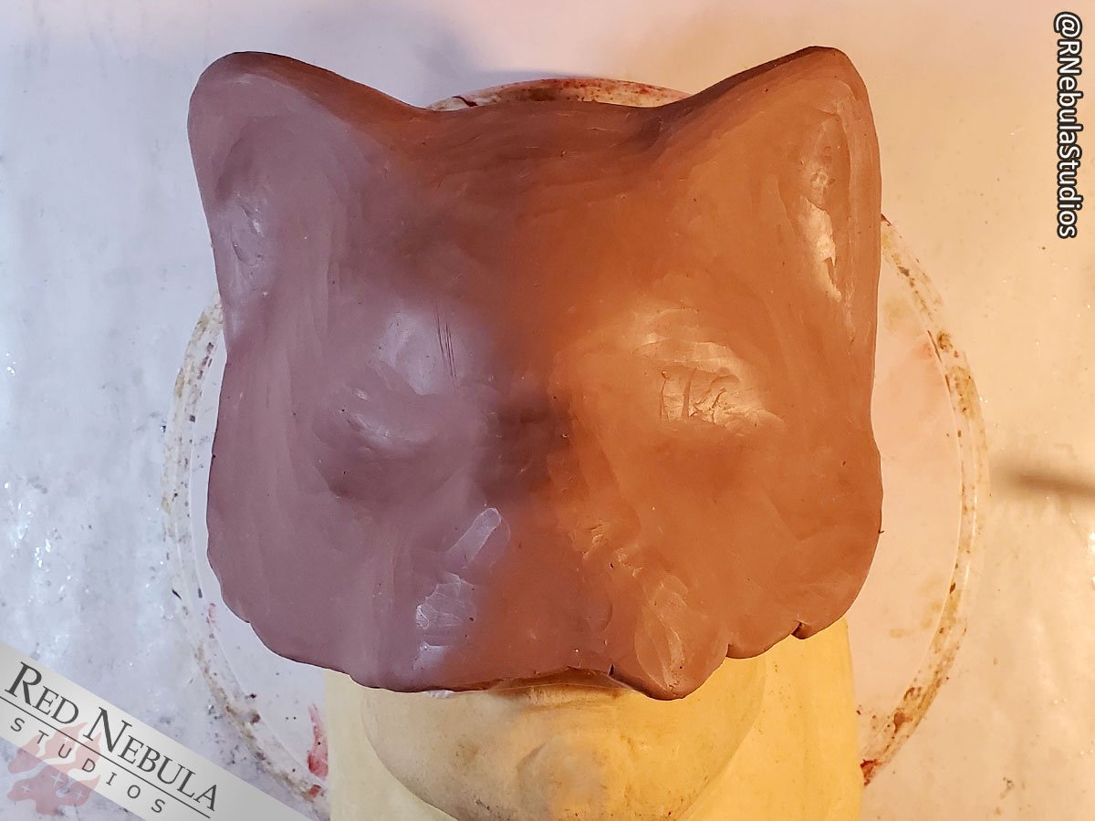 A cat mask covered in a layer of clay in preparation for being made into a matrix mold.
