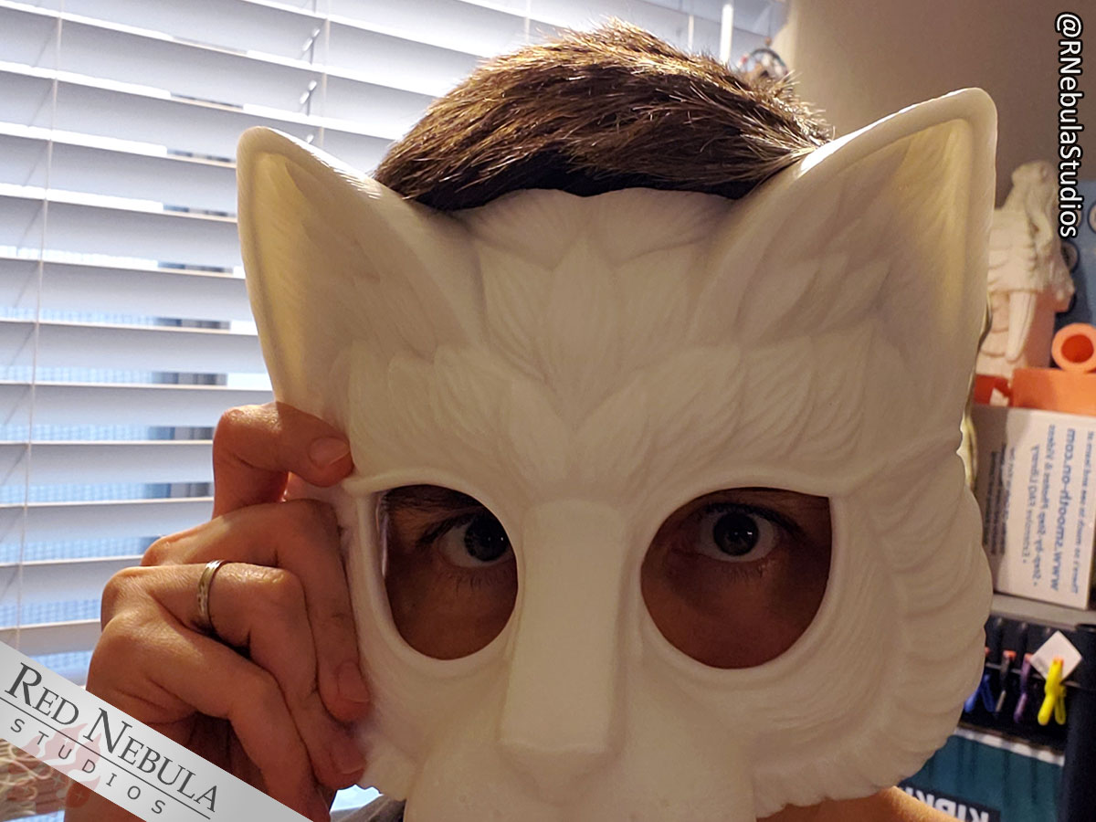 A partially cut-off close-up of a woman holding a white cat mask up to her face.